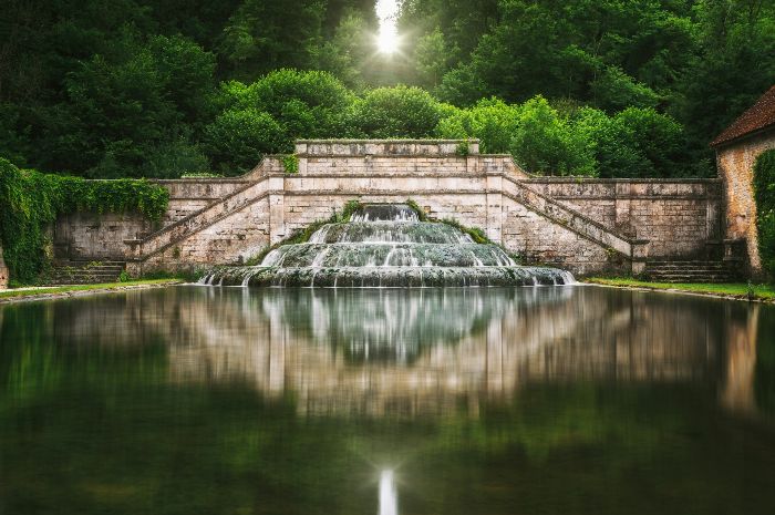 The tranquil beauty of a grand tiered fountain set against a lush backdrop, highlighting the aesthetic enhancement a water feature brings to outdoor spaces.