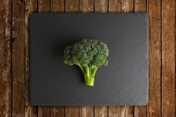 A single head of broccoli placed on a dark slate against a rustic wooden background, symbolizing the focus on understanding the stages of broccoli growth in cultivation.