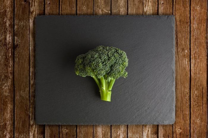 A single head of broccoli placed on a dark slate against a rustic wooden background, symbolizing the focus on understanding the stages of broccoli growth in cultivation.