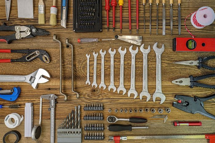A meticulously organized array of essential hand tools laid out on a wooden surface, showcasing a variety of wrenches, screwdrivers, pliers, and measuring tools necessary for every homeowner's toolkit.