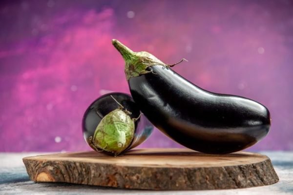 Two fresh eggplants on a wooden cutting board, with a vibrant purple background, illustrating the stages of growth and development in eggplant cultivation.