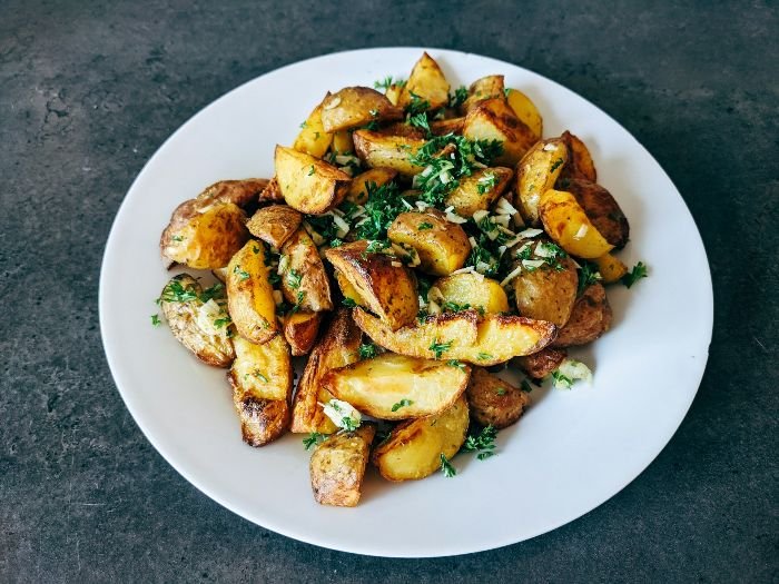 A plate of roasted potatoes garnished with parsley, epitomizing the potato's culinary versatility around the world.