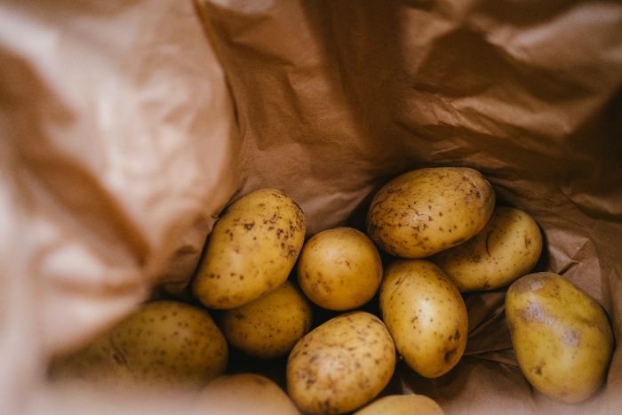 A collection of freshly harvested sweet potatoes nestled in a brown paper bag, showing their smooth, firm skins and natural earthy tones, ready for consumption.