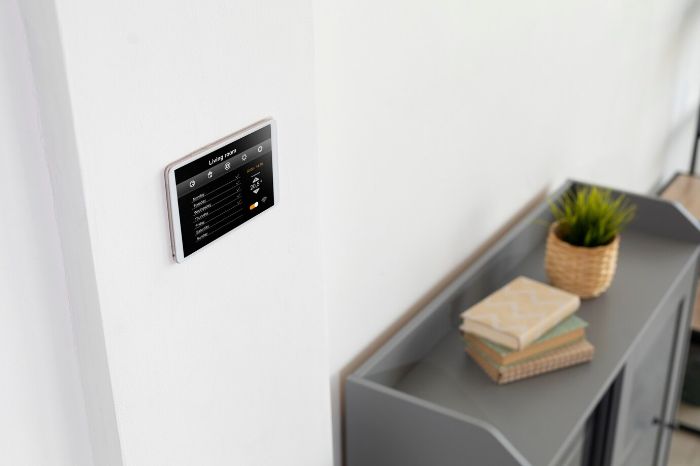 A modern smart thermostat mounted on a white wall above a sleek, gray sideboard in a contemporary living room, displaying energy settings and temperature controls, emphasizing the integration of smart home technology for energy savings.