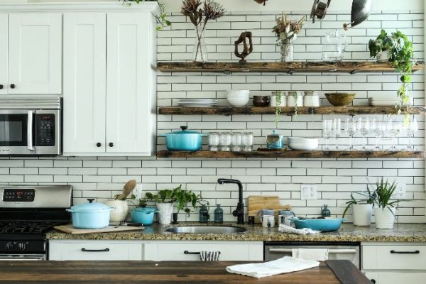 Modern kitchen showcasing efficient use of vertical space with floating wooden shelves against a subway tile backdrop, filled with cookware and plants, optimizing storage in a small kitchen area.