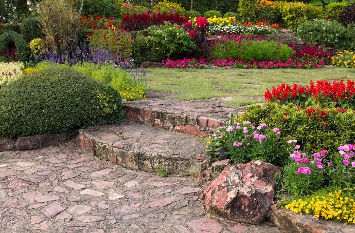 A beautifully landscaped garden with stone pathways, colorful flower beds, and various plants, illustrating the importance of assessing your space before planning your garden layout and plant choices.
