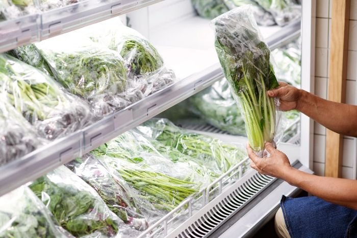 A person handling a bag of fresh vegetables stored in an organized freezer, illustrating techniques to avoid freezer burn by using airtight bags or containers and proper labeling to maintain freshness.
