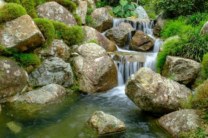 Naturalistic garden waterfall with rocks and lush greenery, emphasizing the need for professional consultation when facing complex issues with garden water features to ensure long-term functionality and enjoyment.