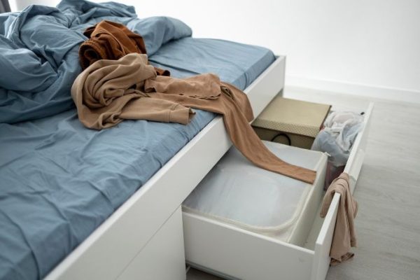 A cluttered under-bed storage area with drawers and clothing, illustrating the need for creative under-bed storage solutions.