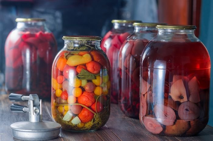 Jars of canned vegetables and fruits on a wooden table, accompanied by canning tools like a pressure canner, illustrating the must-have tools and supplies for safe home canning.
