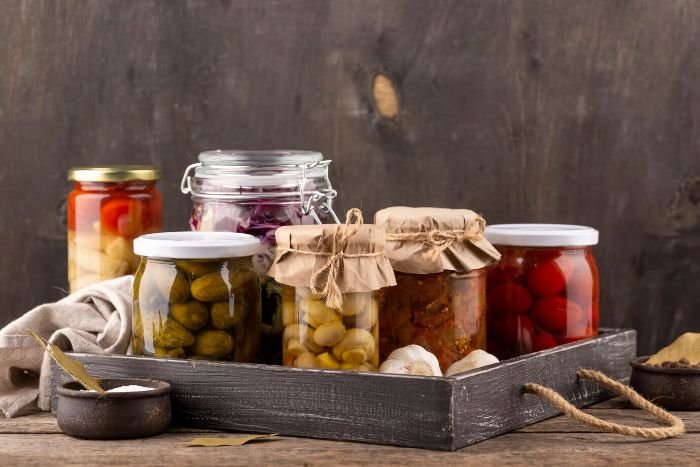 Assorted jars of home-canned vegetables neatly arranged on a wooden tray, showcasing the successful completion of the canning process.