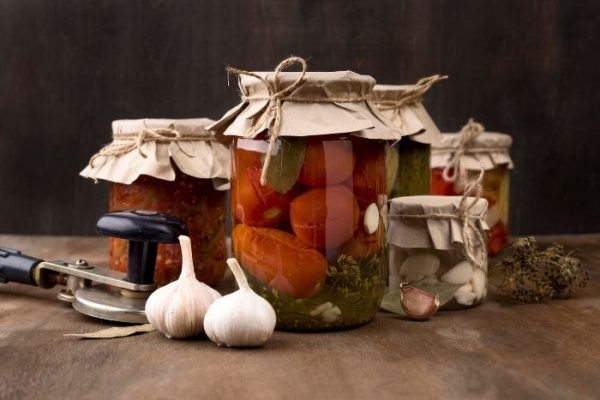 Jars of home-canned vegetables and garlic bulbs on a wooden table, demonstrating the essentials of safe preservation through home canning.