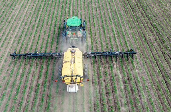 A tractor spreading fertilizer across a large, evenly planted field, illustrating the essential role of fertilizers in gardening and agriculture to enhance plant growth and productivity.