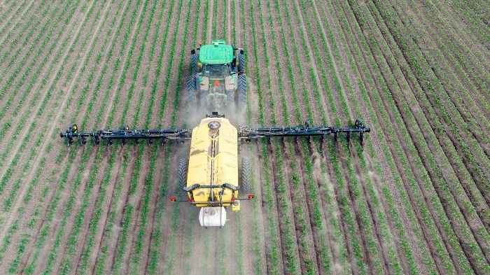 A tractor spreading fertilizer across a large, evenly planted field, illustrating the essential role of fertilizers in gardening and agriculture to enhance plant growth and productivity.