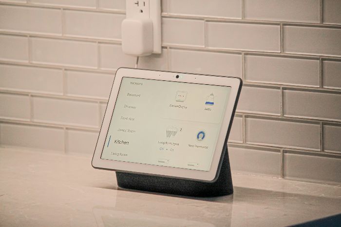 A smart home control tablet displayed on a kitchen counter with a sleek white tile background, showcasing various control options like thermostat settings and device connectivity for efficient home management.