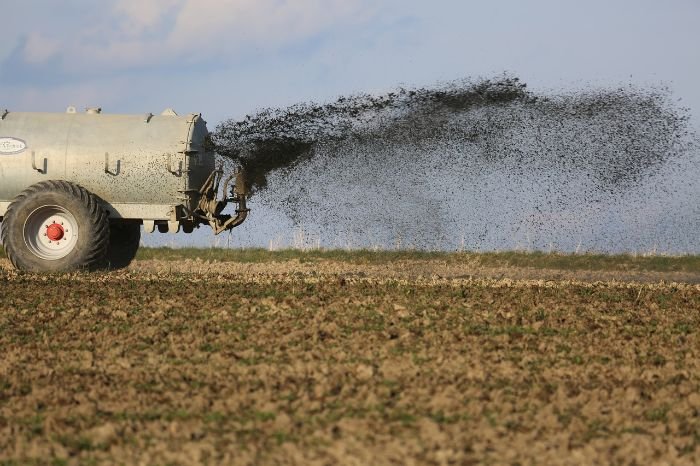 A tractor spreading fertilizer on a field, illustrating the comparison between organic and synthetic fertilizers in agriculture.