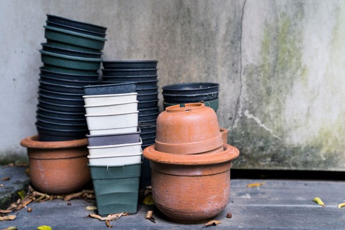 Stacked various pots including clay and plastic containers against a rustic background, illustrating the variety of materials available for gardening and their impact on plant health.
