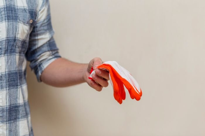 A person holding a pair of orange and white gardening gloves, illustrating the best materials for specific gardening tasks such as leather for strength, cotton for comfort, and rubber for wet or chemical tasks.