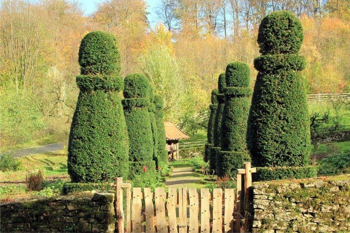 A beautifully landscaped garden with uniquely shaped boxwood topiaries lining a pathway, showcasing creative uses of boxwoods in garden landscaping to add structure and visual interest.