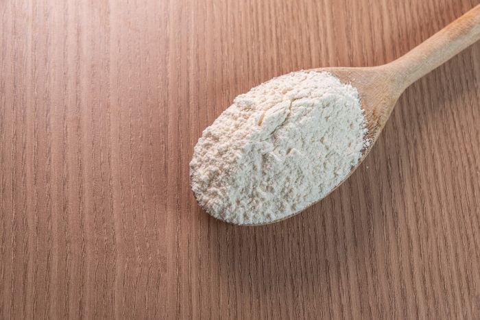 A wooden spoon filled with diatomaceous earth powder on a wooden table, illustrating its use as a natural method for controlling aphids by drying them out.