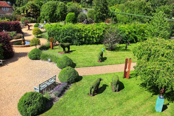 An expansive garden seamlessly blending with its surroundings, featuring sculpted topiary and a meandering gravel path, illustrating effective integration of design elements with the natural landscape.
