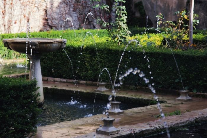 A garden with a decorative water feature, including fountains and a small pond, surrounded by lush greenery and hedges, illustrating the multi-season appeal of adding water features to enhance the beauty and tranquility of the garden.