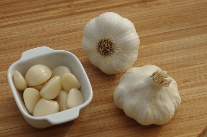 Garlic bulbs and peeled cloves on a wooden surface, illustrating the planting stage of garlic and the importance of selecting the right garlic varieties.