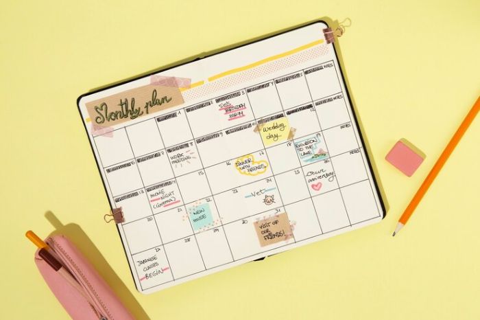 A calendar planner open on a yellow surface, filled with handwritten notes and colorful sticky notes, symbolizing the importance of planning and preparing for the next gardening year in December.