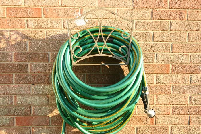 A green garden hose neatly coiled on a decorative wall-mounted hanger, illustrating the importance of proper storage and handling to ensure the hose's longevity and prevent damage.