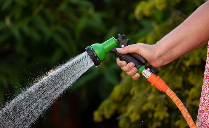 A person using a garden hose with a spray nozzle, highlighting the importance of selecting the right fittings for durability, compatibility, and ease of use to match your garden's needs.