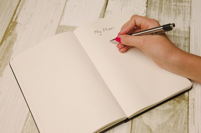 A person writing "My Plan" in a notebook, illustrating the process of setting goals and creating a garden plan for the upcoming gardening season.