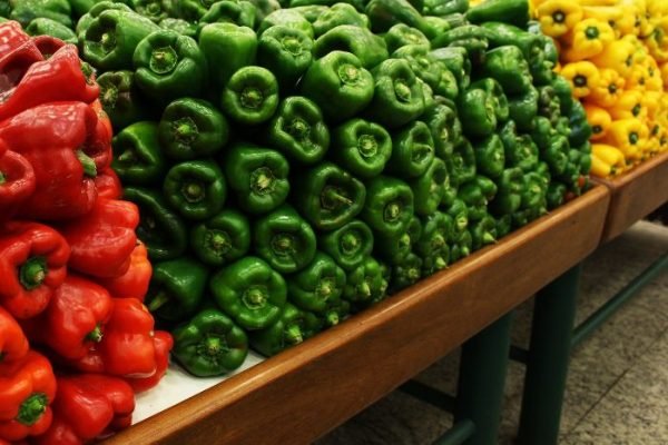 A vibrant display of red, green, and yellow bell peppers stacked on a market shelf, showcasing the variety and health benefits of bell peppers as a rich source of vitamins and antioxidants.