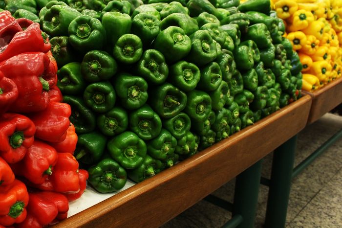 A vibrant display of red, green, and yellow bell peppers stacked on a market shelf, showcasing the variety and health benefits of bell peppers as a rich source of vitamins and antioxidants.