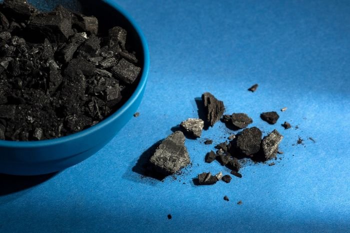Close-up of biochar pieces in a bowl and scattered on a blue surface, illustrating its benefits as a soil amendment for sustainable farming.