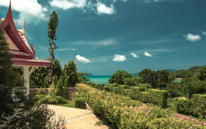 A lush garden near a seaside with various plants and a traditional pavilion, illustrating the challenges of maintaining a garden in windy conditions.
