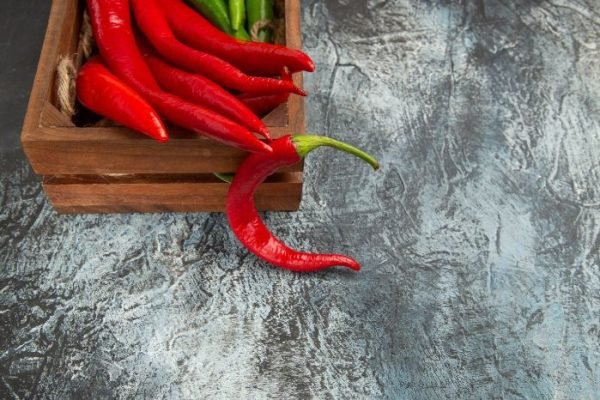 Red chili peppers in a wooden crate on a textured surface, showcasing their vibrant color and health benefits, including boosting metabolism and adding spice to your diet.