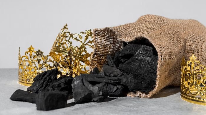Burlap bag spilling biochar chunks surrounded by golden crowns, symbolizing the myths and truths about biochar's benefits and uses.