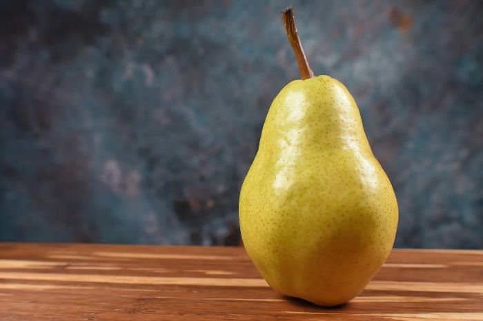 Ripe pear on a wooden surface, highlighting the benefits of growing fiber-filled fruits like pears for improved digestive health.