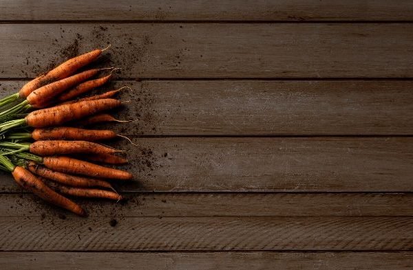 A bunch of freshly harvested carrots on a wooden surface, highlighting the health benefits of carrots beyond just vision support.