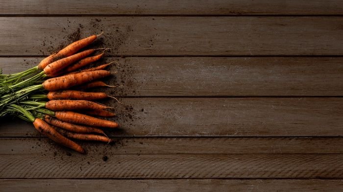 A bunch of freshly harvested carrots on a wooden surface, highlighting the health benefits of carrots beyond just vision support.