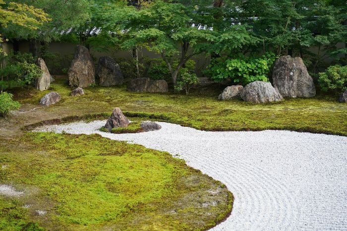A serene rock garden with large rocks, green moss, and a gravel path, showcasing the use of rocks and hardscaping elements to create natural beauty and functional pathways.