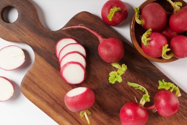 Freshly sliced radishes on a wooden cutting board with whole radishes around, highlighting the crunchy texture and detoxifying benefits of this nutritious vegetable.