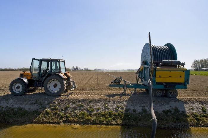 Drip irrigation system setup in a field with a tractor and irrigation equipment, demonstrating efficient water delivery directly to the plant roots.