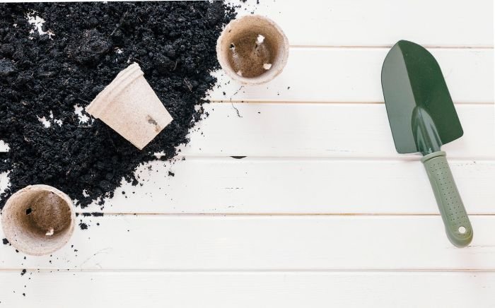 Gardening tools and biochar soil mixture on a white wooden table, illustrating the use of biochar to enhance soil health and improve long-term environmental sustainability.