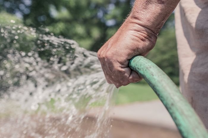 Close-up of a person's hand holding a garden hose, demonstrating effective water management techniques for soil conservation in permaculture.