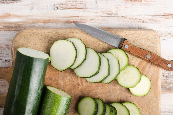 Sliced zucchini on a wooden cutting board with a knife, highlighting the low-calorie, high-nutrient benefits of zucchini for weight management.