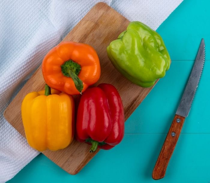 Four bell peppers in different colors (orange, yellow, red, and green) on a cutting board, illustrating their unique flavors and best uses in various recipes like salads, stir-fries, soups, and pizzas.