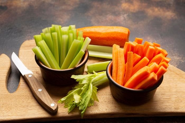 Chopped celery and carrot sticks in bowls on a cutting board, showcasing the versatile culinary uses and preparation of carrots.