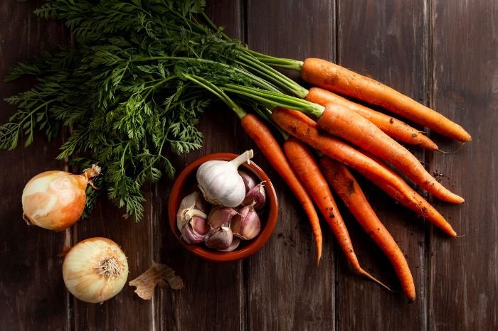 Fresh carrots with onions and garlic on a wooden table, showcasing their role in boosting the immune system and providing essential nutrients.