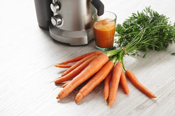 Fresh carrots beside a glass of carrot juice and a juicer, highlighting their role in weight management and overall health benefits.